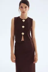 Top sin mangas color marrón oscuro, con cuello redondo y abertura frontal cerrada con tres botones dorados en forma de concha de mar.