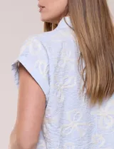 Camisa celeste con bordado floral en color crudo, de corte semi holgado, cuello camisero, manga corta japonesa con dobladillo y cierre frontal de botones.