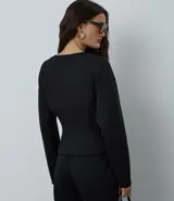Campera femenina de punto roma en color negro, con diseño acinturado y efecto peplum. Presenta cierre frontal con cremallera metálica, escote en V y bolsillos delanteros.