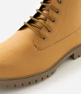 Bota estilo worker de caña media con acabado tipo nobuck. Presenta puntera redondeada, cuello acolchado en contraste, cierre con cordones y ojalillos metálicos. Cuenta con suela dentada de goma para mayor tracción.