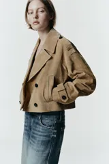 Trench corto de Zara confeccionado en piel de ante, con cuello de solapa, cierre frontal cruzado con botones, mangas largas con trabillas y bolsillos delanteros de vivo.