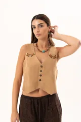 Chaleco de gamuza color beige con estilo western, presenta cierre frontal con botones y detalles de ojalillos metálicos con cordones de cuero entrelazados en la parte superior del frente.