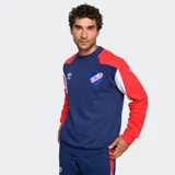 Buzo de entrenamiento Umbro, color azul marino, con diseño de bloques de color en hombros y mangas (rojo y blanco). Presenta el logo de Umbro y el escudo del Club Nacional de Football en el pecho.