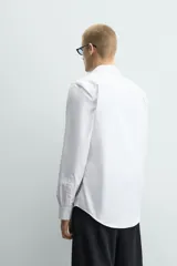 Camisa de corte slim fit confeccionada en tejido de algodón con textura. Presenta cuello italiano, manga larga con puños abotonados y cierre frontal mediante botonadura.