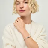 Pulsera de aleación de metales bañados en plata, compuesta por dos tiras de cuentas metálicas y detalles de cuero marrón oscuro, con un adorno central de dos gotas plateadas.