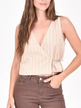 Chaleco sin mangas de color beige con rayas verticales blancas. Presenta un diseño cruzado tipo wrap con escote en V y ajuste mediante lazo lateral.