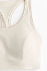 Top deportivo color beige con espalda nadadora, escote redondo y banda elástica inferior.