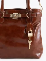 Bandolera de cuero vacuno en color marrón, con manija de mano, correa regulable, cierre superior y detalles de herrajes metálicos dorados, incluyendo un candado y una llave decorativos.