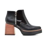 Botín de cuero negro con puntera redondeada y cierre lateral con cremallera. Tiene un tacón ancho de madera y plataforma.