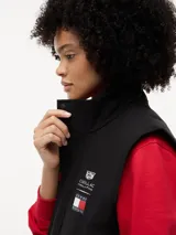 Chaleco negro con cuello chimenea, cierre de cremallera oculto con botones a presión y dos bolsillos laterales ribeteados. Presenta logos bordados en el pecho de Tommy Hilfiger y Cadillac Formula 1 Team.