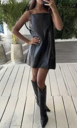 Vestido corto negro de cuero italiano con breteles finos regulables y pequeños tajos laterales y trasero.