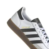 Championes Adidas Handball Spezial con diseño clásico de perfil bajo. Presentan una base de cuero blanco con las icónicas tres rayas laterales en negro, refuerzo de gamuza gris en la puntera y suela de goma color caramelo.