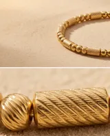 Pulsera tipo esclava rígida de acero con baño de oro, con diseño de eslabones texturizados y esferas lisas intercaladas.