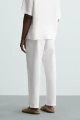 Pantalón de corte relajado color beige confeccionado en tejido de mezcla de algodón y lino. Posee cintura elástica ajustable con cordón, bolsillos frontales y bolsillos traseros de vivo.