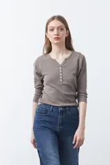 Remera de manga larga color beige, confeccionada en algodón, con escote en V y cartera corta de botones blancos.