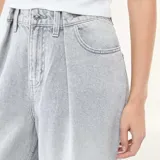 Jean de corte wide leg y tiro alto, confeccionado en denim de color gris lavado. Presenta pinzas en la cintura, cierre frontal con botón y bolsillos laterales.