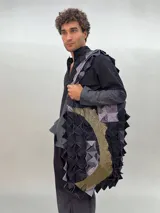 Bolso de gran tamaño confeccionado artesanalmente con técnica de ensamblado de cuadrados de lana merino afiltrada en tonos violeta y gris. Presenta un diseño texturizado y voluminoso, con forro interior de algodón y bolsillo con cierre.