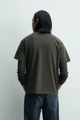 Camiseta relaxed fit color gris oscuro, confeccionada en tejido ligero de algodón con elasticidad. Presenta cuello redondo y manga ranglán corta.