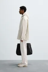 Sobrecamisa de corte oversized confeccionada en tejido compacto de algodón. Presenta cuello subido con capucha ajustable mediante cordones, cierre frontal con botonadura, manga larga con puños abotonados y dos bolsillos de plastrón en la parte frontal.