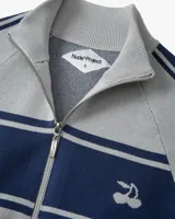 Jersey de punto con cierre frontal de cremallera y cuello alto. Presenta un diseño bicolor en gris y azul marino, con franjas horizontales en el pecho, detalles laterales en las mangas y logo de cerezas bordado.