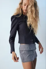 Blazer corta de color azul marino, con cuello solapa y cierre frontal con botones. Cuenta con manga larga con frunces en los hombros.