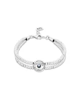 Pulsera de doble cadena formada por pequeñas esferas metálicas bañadas en plata, con un dije central circular en forma de ojo que contiene un cristal azul en el centro.