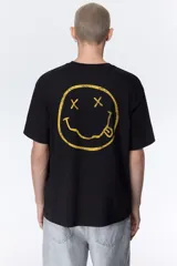 Remera de algodón color negro con cuello redondo y mangas cortas. Presenta un estampado frontal con el logo de la banda Nirvana en color amarillo y una imagen en blanco y negro del concierto Live at Reading.