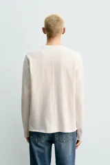 Camiseta de manga larga con corte relajado, confeccionada en tejido de algodón compacto. Presenta cuello redondo y detalle de costura en el centro de la espalda.