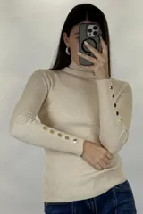 Polera de hilo blanca de cuello alto y manga larga, con detalle de botones dorados en los puños. Tejido de punto acanalado ajustado al cuerpo.