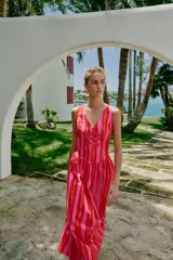 Vestido largo sin mangas con escote en pico y tirantes anchos. Presenta un diseño de rayas verticales en tonos fucsia y rojo, con detalle de falsos botones frontales y cierre de cremallera oculto en la espalda.
