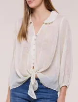 Blusa confeccionada en gasa semitransparente con sutil acabado plisado y estampado floral en tonos suaves. Presenta cuello solapa redondeado, escote en V y botonadura frontal. Mangas largas con puños elásticos y ruedo anudado en la parte inferior frontal.