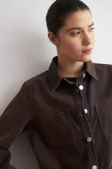 Sobrecamisa de jean con acabado simil terciopelo en color marrón oscuro, de corte recto, manga larga, cuello clásico y cierre frontal con botones metálicos.