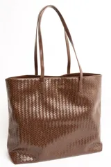 Bolso tipo shopper color marrón de cuero sintético con diseño trenzado. Cuenta con doble asa de hombro y placa metálica con el logo de la marca en el frente.
