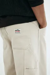 Pantalón worker de sarga de algodón gruesa color beige, con piernas rectas y corte relajado. Presenta cintura clásica con cierre de botón, bolsillos al bies, bolsillo monedero, bolsillos traseros, trabilla funcional en un lateral y bolsillo cargo dividido en dos en el otro.