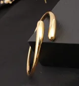 Pulsera tipo brazalete abierto, color dorado, con extremos gruesos y redondeados.