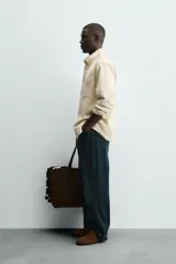 Sobrecamisa de corte regular confeccionada en tejido de algodón color beige. Presenta cuello de solapa, manga larga con puños abotonados y un bolsillo de parche en el pecho. Se caracteriza por sus pespuntes decorativos en contraste y cierre frontal con botones.