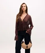 Cartera tipo baguette de diseño curvo, confeccionada en gamuza sintética color beige con detalles en cuero marrón oscuro. Presenta costuras decorativas en los bordes, una correa ajustable y cierre frontal con hebilla metálica dorada.