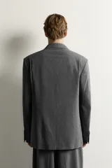 Blazer gris de corte relaxed fit con diseño de raya diplomática, cuello con solapas de pico, doble botonadura cruzada y bolsillos con solapa en la cadera.