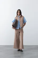 Chaleco de pana color marrón oscuro, con cuello camisero, cierre frontal de botones metálicos dorados y dos bolsillos frontales con detalle de bordado geométrico.