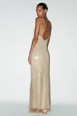 Vestido largo color dorado, confeccionado en tejido tipo red con aplicación de strass, escote pico y tirantes finos. Incluye forro interior y cierre en espalda con cremallera oculta en costura.