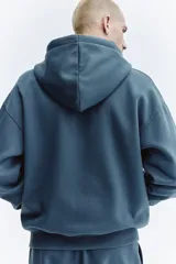 Campera con capucha de corte oversized, confeccionada en tejido de mezcla de algodón con interior suave. Presenta cierre frontal, hombros caídos, cordón ajustable en la capucha y bolsillos tipo canguro. Puños y bajo acanalados.
