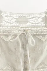 Top crop de algodón con escote cuadrado y tirantes anchos. Presenta bordados florales, aplicaciones de encaje y cierre frontal con botones y lazadas.