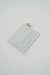 Tarjetero metálico color plateado con textura rugosa y costuras visibles. Incluye una pequeña etiqueta de marca en la parte superior.