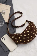 Bolso pequeño de hombro con forma de media luna, color negro, decorado con tachas redondas doradas. Cuenta con una correa ajustable y herrajes dorados.