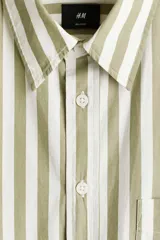 Camisa de popelina de algodón con diseño a rayas en color verde militar y blanco, cuello inglés, cierre frontal de botones, bolsillo en el pecho y mangas largas con puños abotonados.