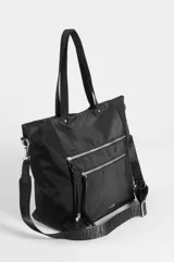 Cartera tipo shopper color beige de nylon, con doble asa de hombro y bolsillos frontales con cierres metálicos y tiradores de cordón negro.