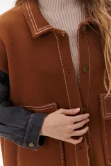 Campera color caramelo con mangas de denim azul oscuro. Presenta cuello alto, cierre frontal con botones, cuatro bolsillos delanteros con solapa y pespuntes blancos decorativos.