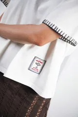 Remera de algodón color azul marino, corte relajado con hombro caído. Presenta cuello redondo blanco y bordado a mano en contraste en los puños de las mangas. Tiene un parche bordado en la parte inferior del frente.