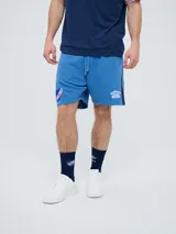 Bermuda deportiva Umbro del Club Nacional de Football, color celeste, con cordón ajustable en la cintura, bolsillos laterales, el escudo del club en una pierna y el logo de la marca en la otra.