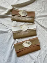 Billetera tipo sobre de ecocuero color beige con textura craquelada y solapa con aplique de cuero liso y botón de guampa.